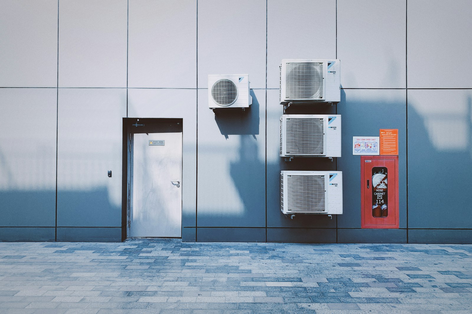Four air conditioning units mounted on a grey panelled wall