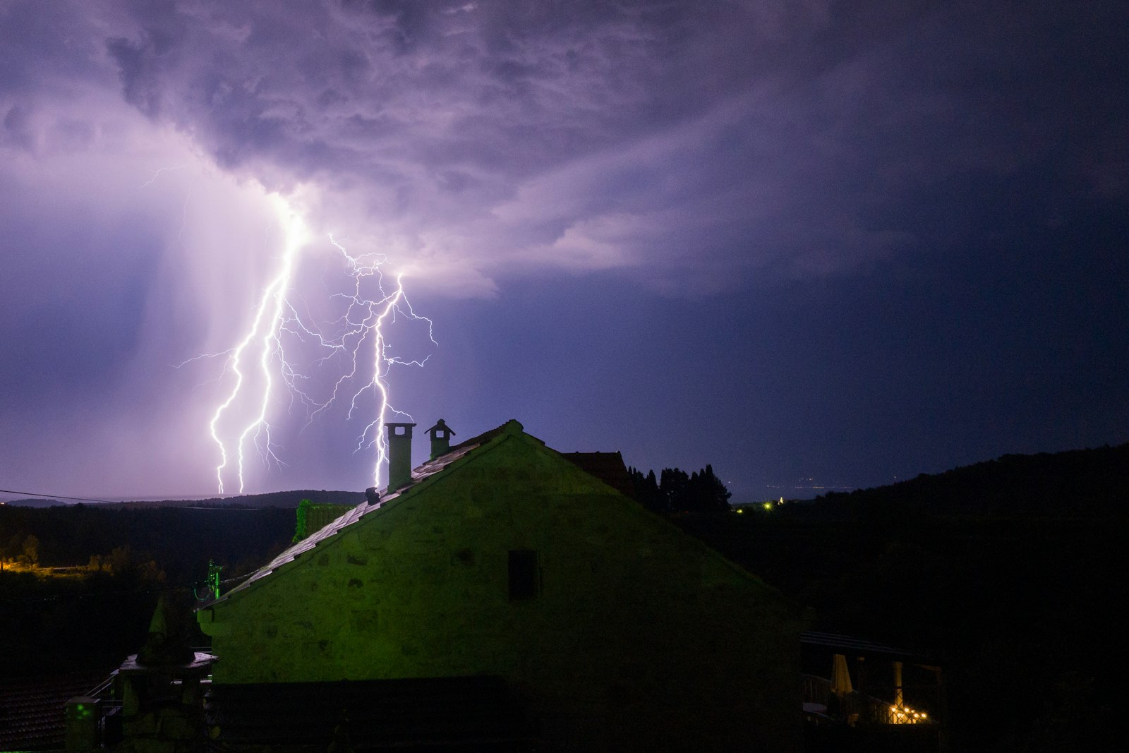 Lightning over a house at night, the kind of storm that sends homeowners searching for a local roofer