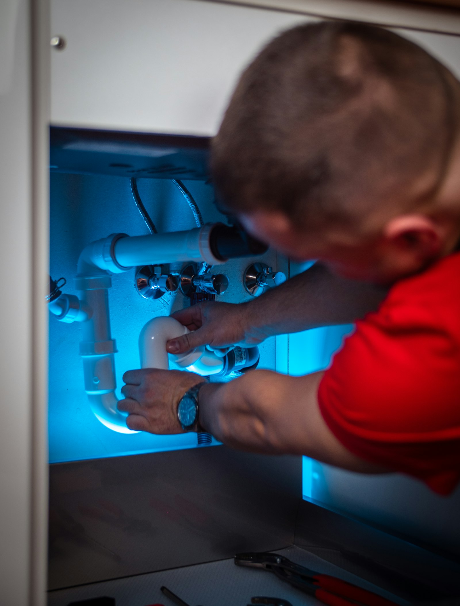 Plumber working under a sink cabinet, the kind of job homeowners ask about before booking a plumbing company